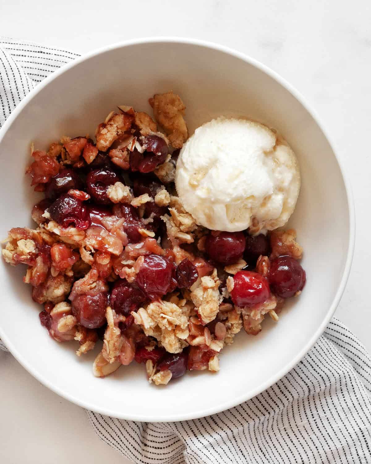 Cherry crumble served with a scoop of vanilla ice cream in a small bowl.