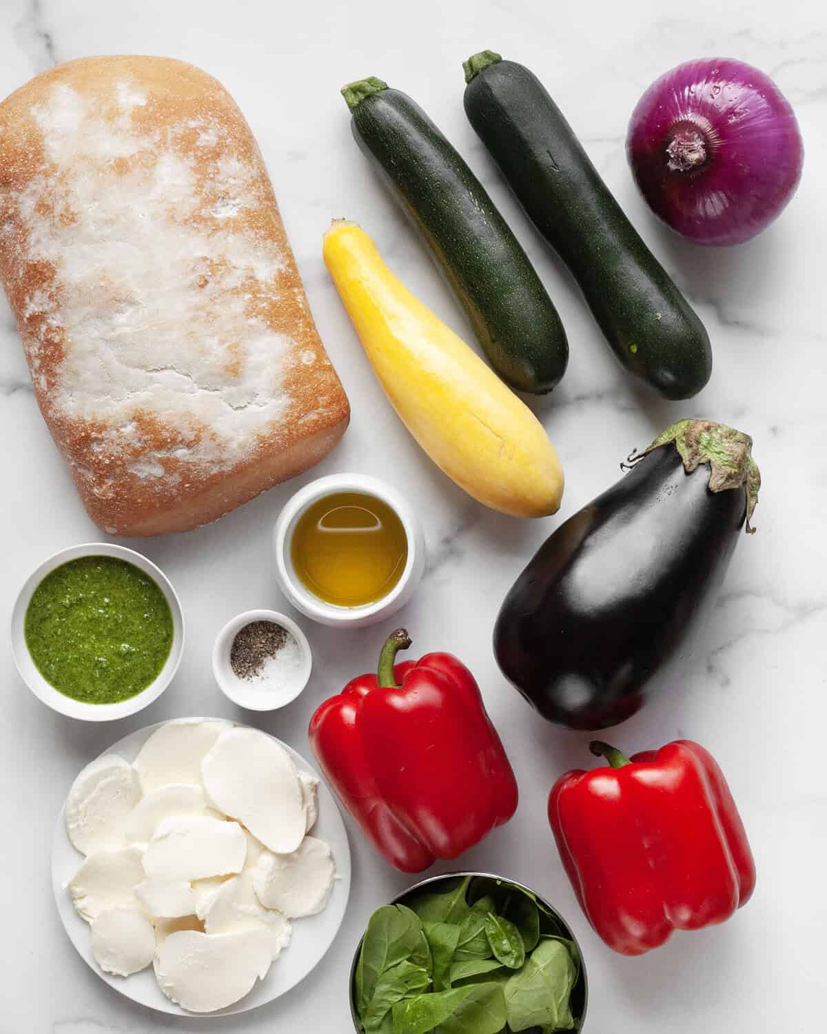 Ingredients including bread, vegetables, pesto, olive oil, salt, pepper and mozzarella.