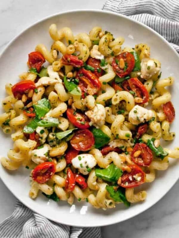 Pesto pasta salad with roasted tomatoes and mozzarella on a plate.