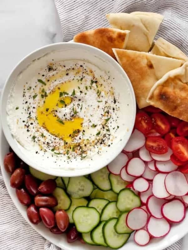 Labneh in a bowl with a platter of pita, tomatoes, radishes, cucumbers and olives