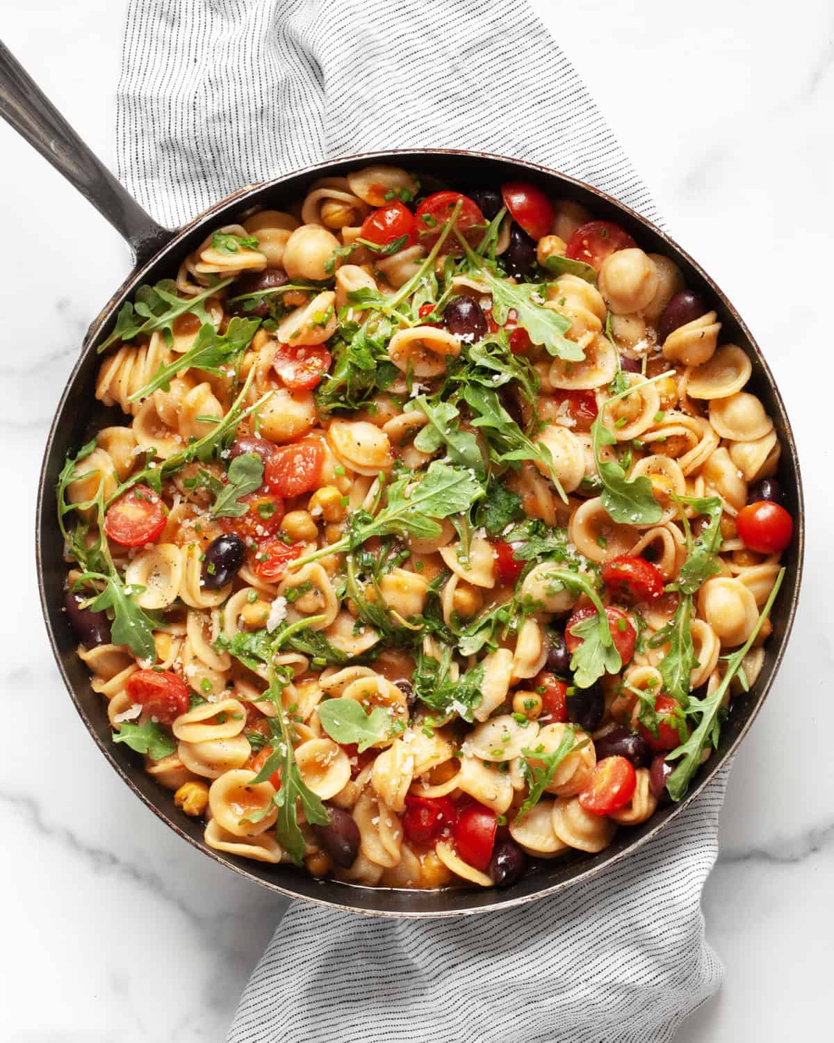 One pan pasta with chickpeas, tomatoes, olives and arugula in a skillet.