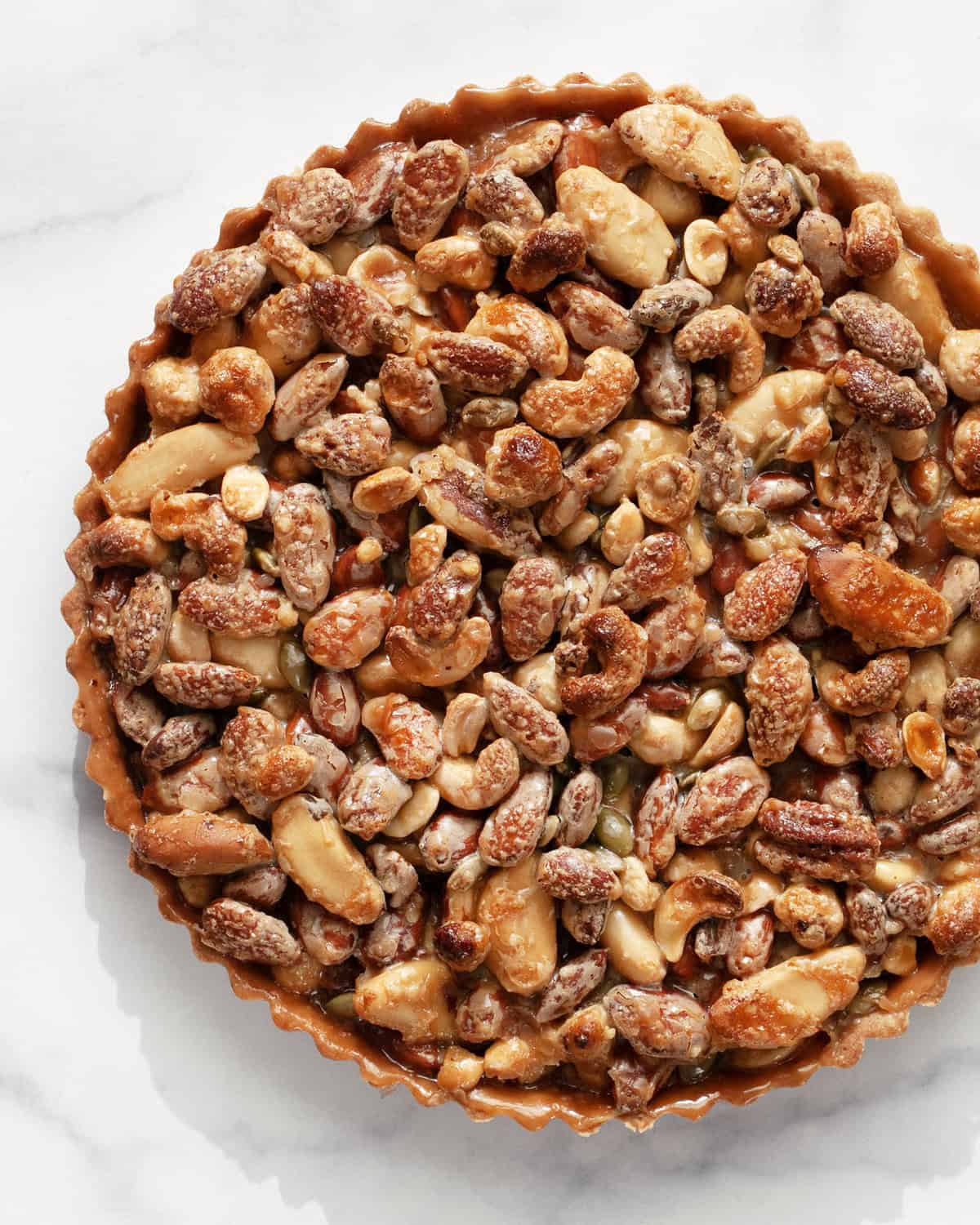 A caramel mixed nut tart on a marble surface.