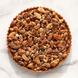 A caramel mixed nut tart on a marble surface.