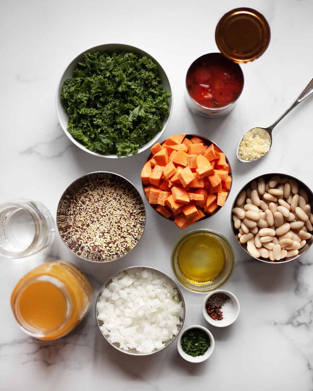 Ingredients for soup including quinoa, sweet potatoes, white beans, kale, tomatoes, olive oil, onions, broth and seasonings.