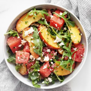 Watermelon salad with peaches, feta, arugula and jalapeño lime dressing in a bowl.