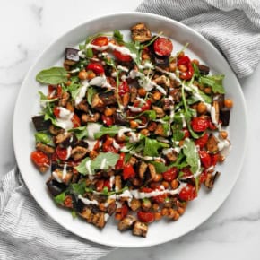 Roasted eggplant, tomatoes and chickpeas drizzled with lemon tahini sauce on a plate.