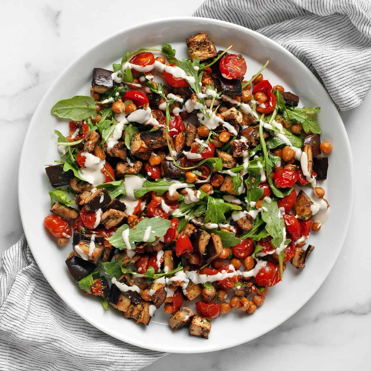 Eggplant, tomatoes and chickpeas drizzled with lemon tahini sauce on a plate.