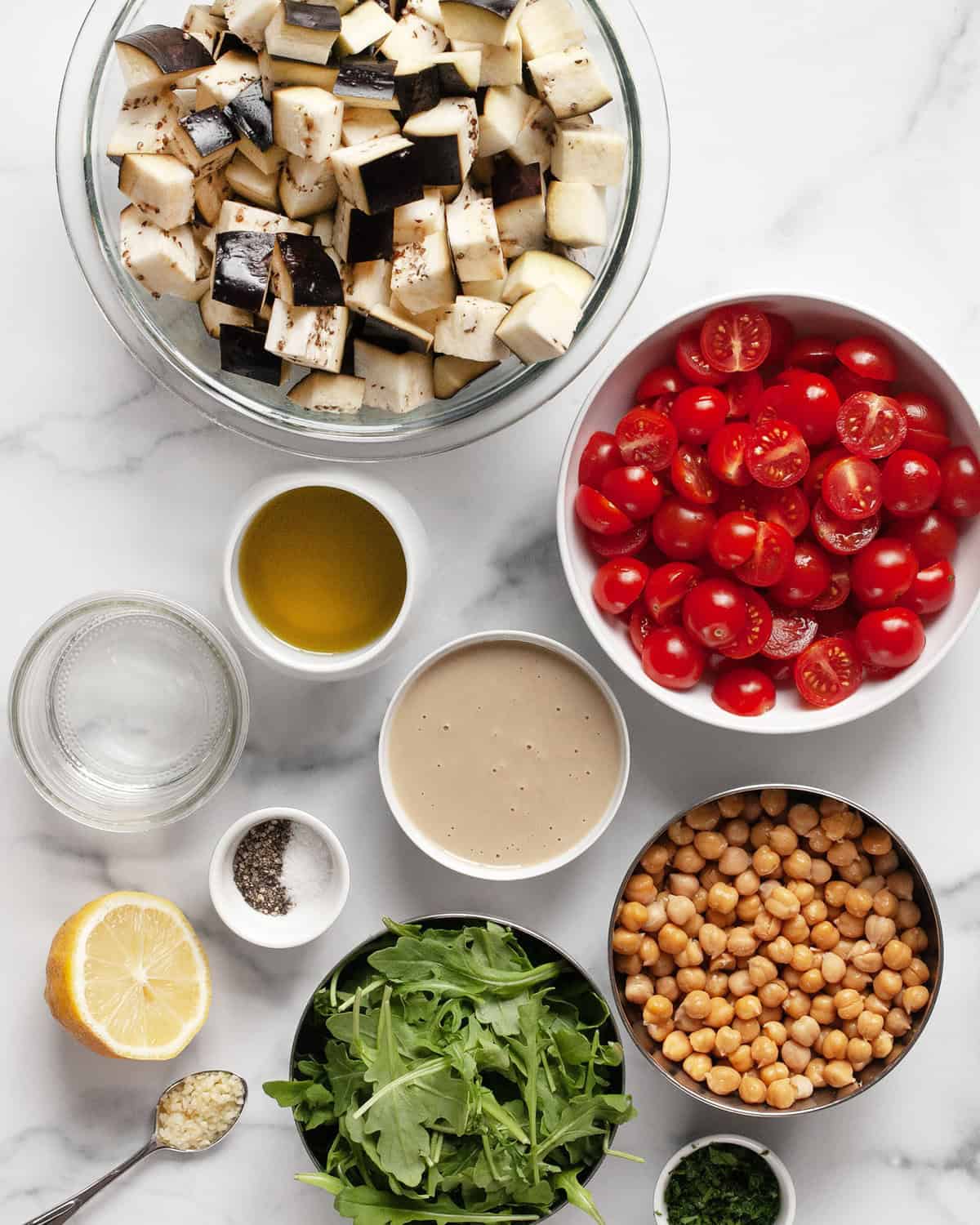 Ingredients including eggplant, tomatoes, chickpeas, arugula, tahini, lemon, parsley, salt and pepper.