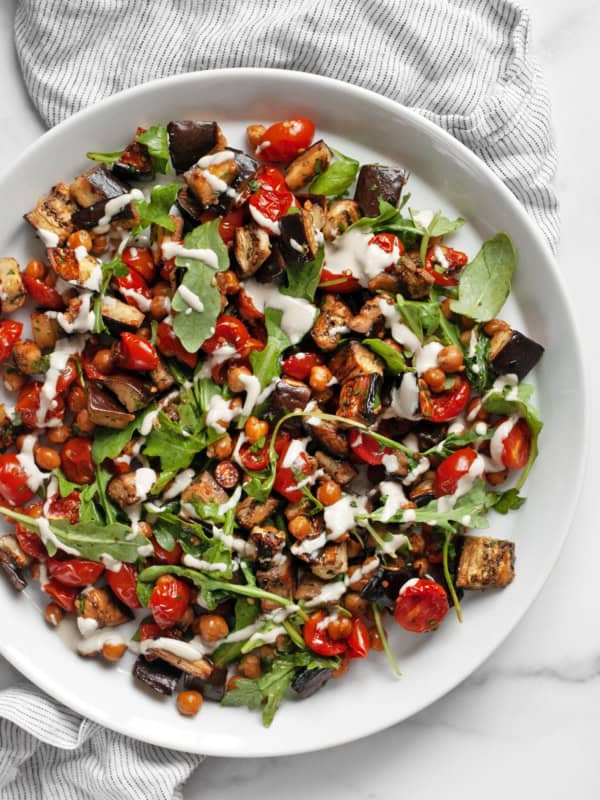 Roasted eggplant, tomatoes and chickpeas drizzled with lemon tahini sauce on a plate.