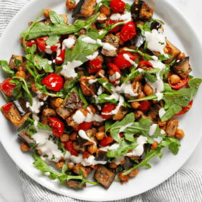 Roasted eggplant, tomatoes and chickpeas drizzled with lemon tahini sauce on a plate.