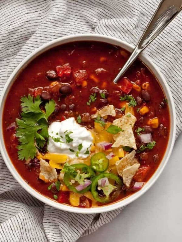 Bowl of black bean chili with tortilla chips, sour cream, cilantro, jalapenos, and cheese.