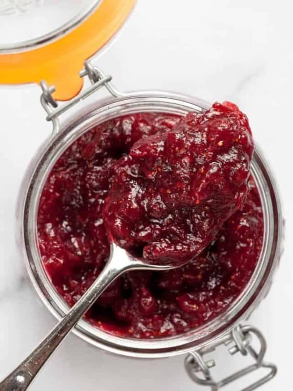 Spoon with cranberry jam sitting on a jar.