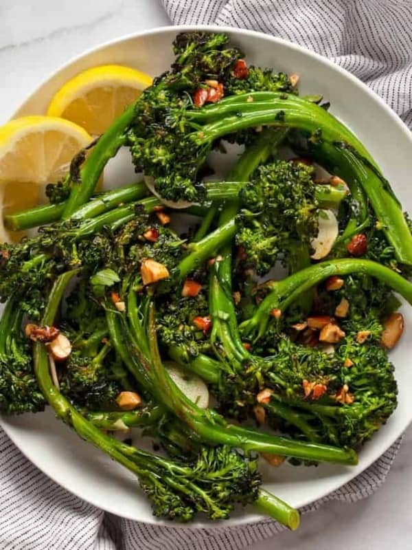 Sauteed broccolini piled on a plate with lemon wedges.