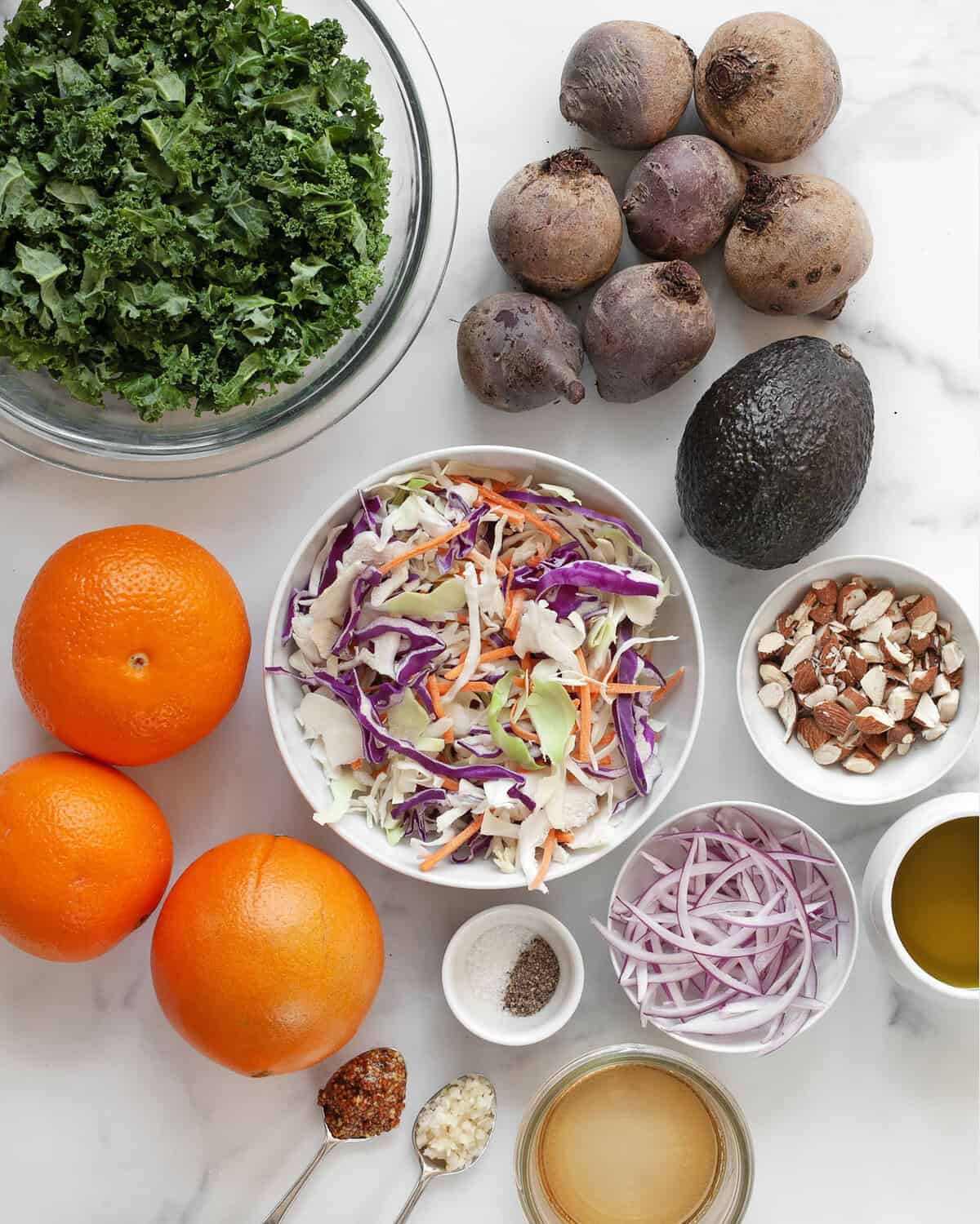 Ingredients including beets, oranges, kale, coleslaw mix, avocado, red onions, almonds, garlic, mustard, vinegar and olive oil.