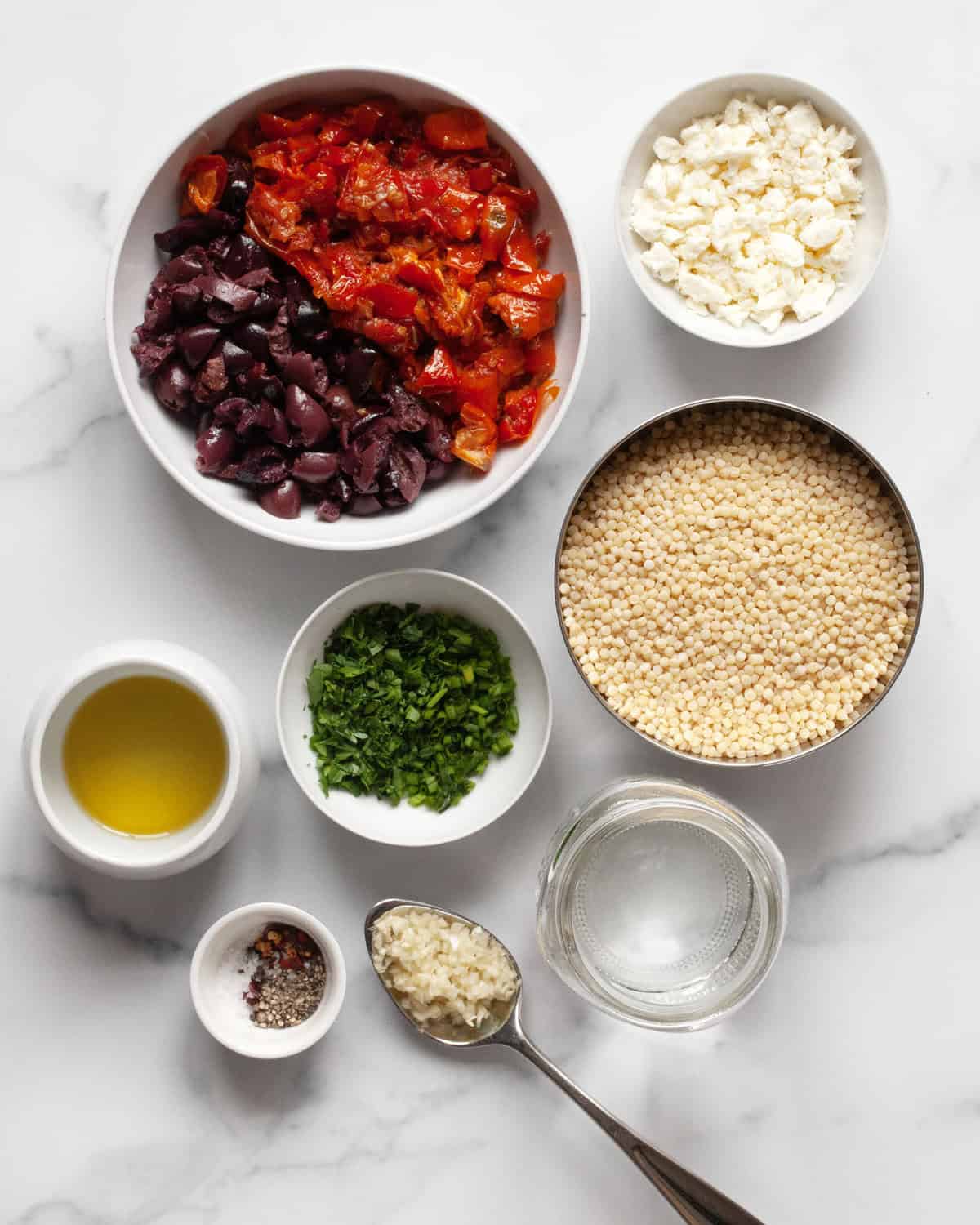 Ingredient including tomatoes, olives, pearl couscous, feta, garlic, olive oil, herbs and spices.