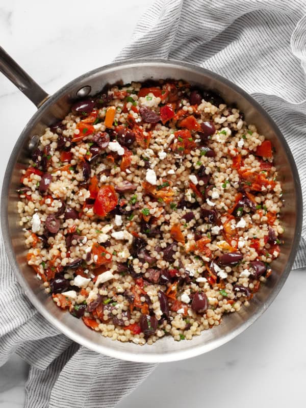 Pearl couscous with tomatoes and olives in a skillet.