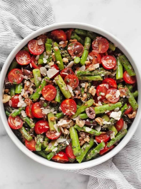 Grilled asparagus salad with tomatoes, olives and walnuts in a bowl.