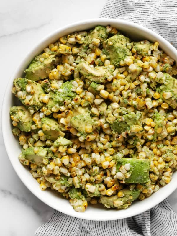 Grilled corn tossed with cilantro pesto and avocados in a bowl.