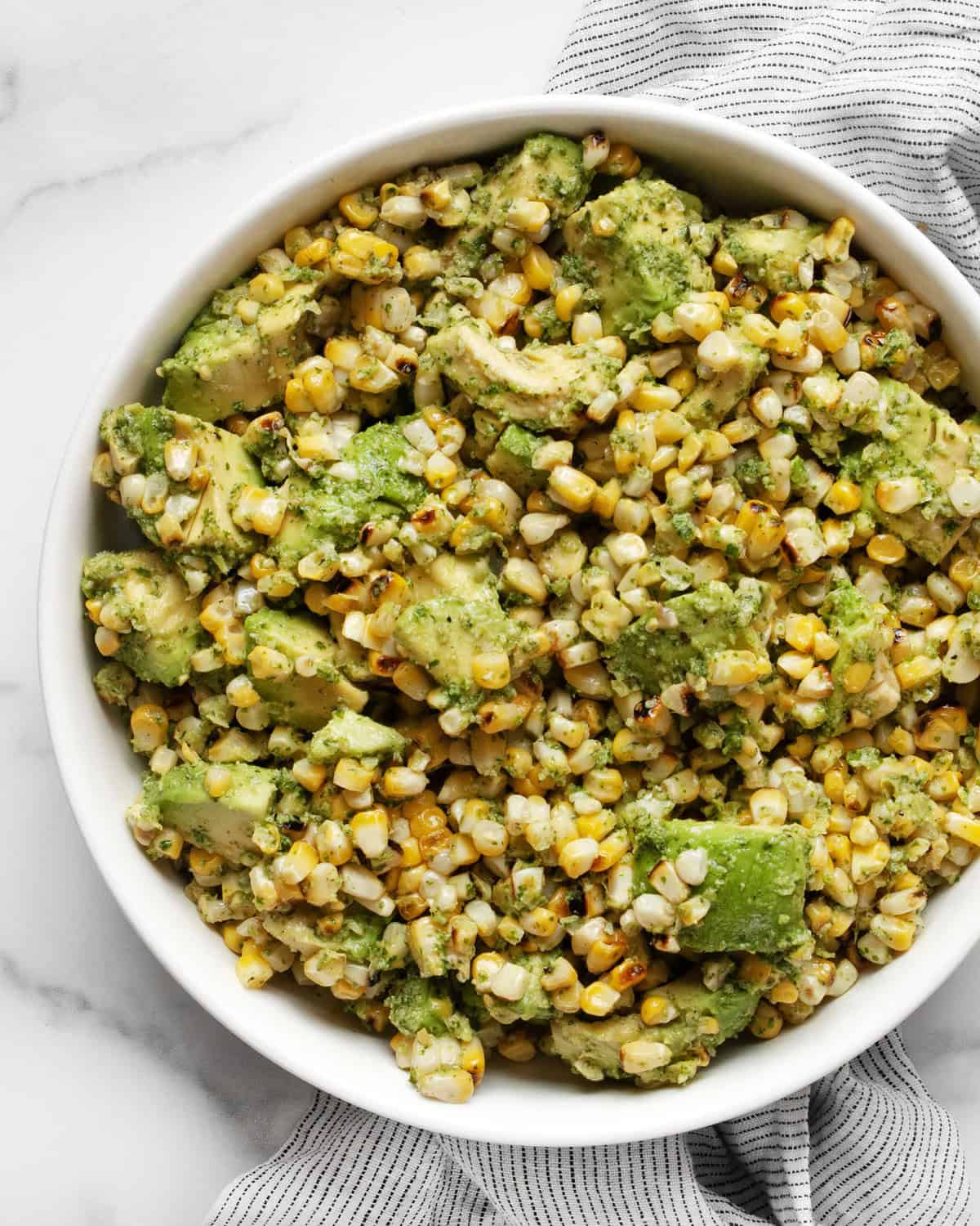 Grilled corn tossed with cilantro pesto and avocados in a bowl.