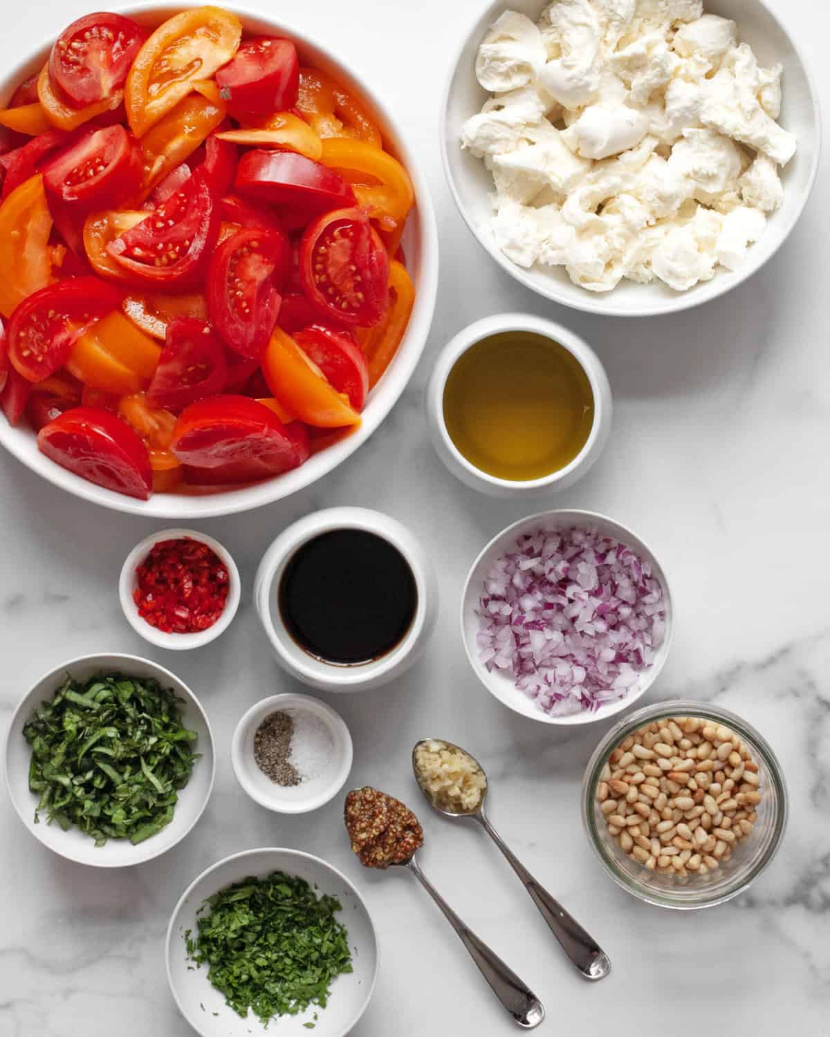 Ingredients for salad including tomatoes, mozzarella, pine nuts, basil, parsley, onions, chilies, balsamic vinegar, olive oil, salt and pepper.