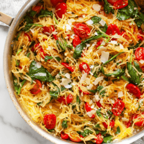 Spaghetti squash with roasted tomatoes and spinach in a skillet.