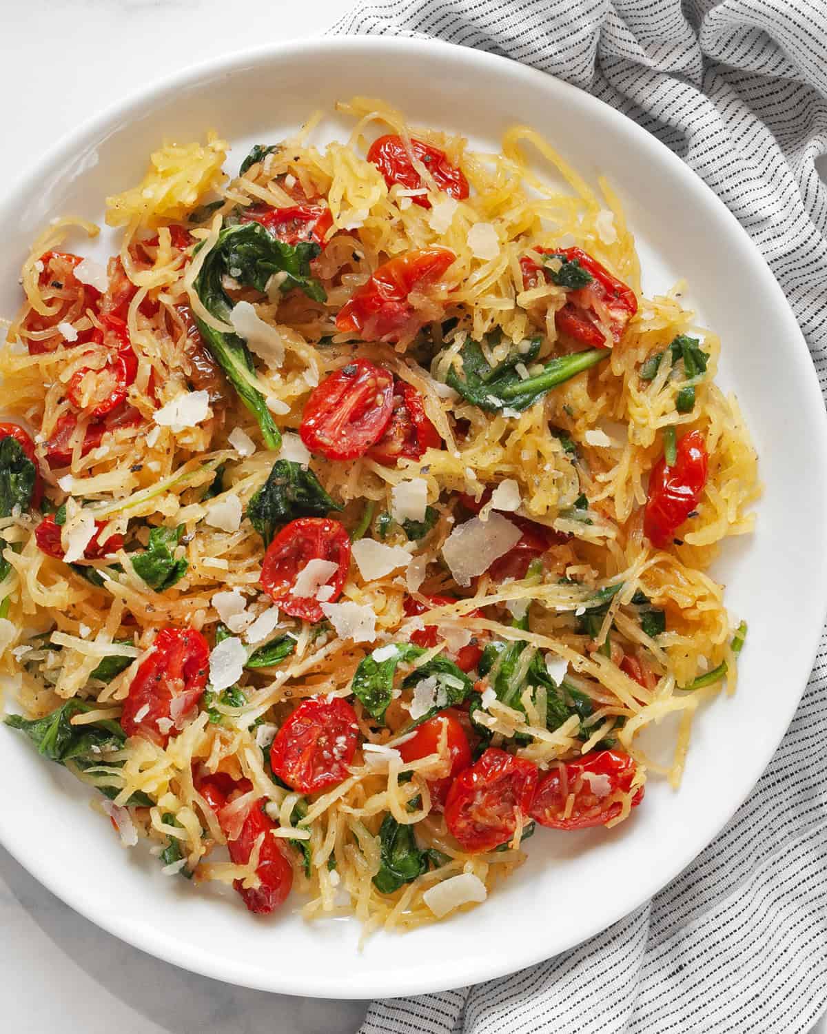 Roasted spaghetti squash with roasted tomatoes and baby spinach on a plate.