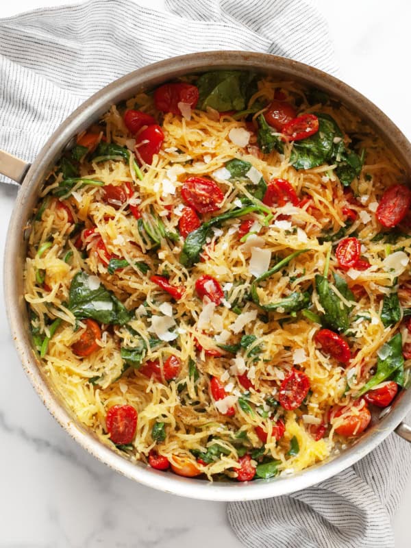 Roasted spaghetti squash with roasted tomatoes and baby spinach in a skillet.