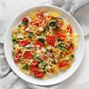 Roasted spaghetti squash with roasted tomatoes and baby spinach on a plate.