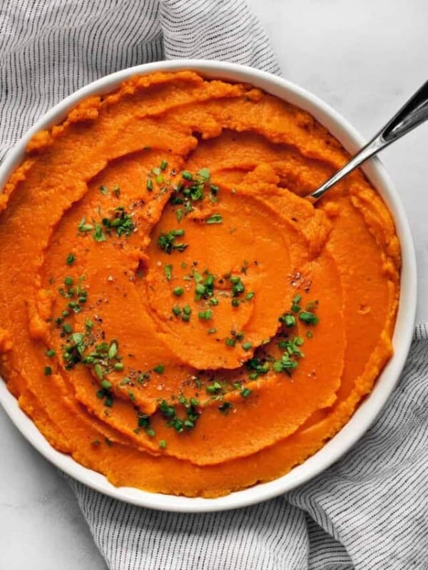 Mashed sweet potatoes in a bowl with fresh herbs.