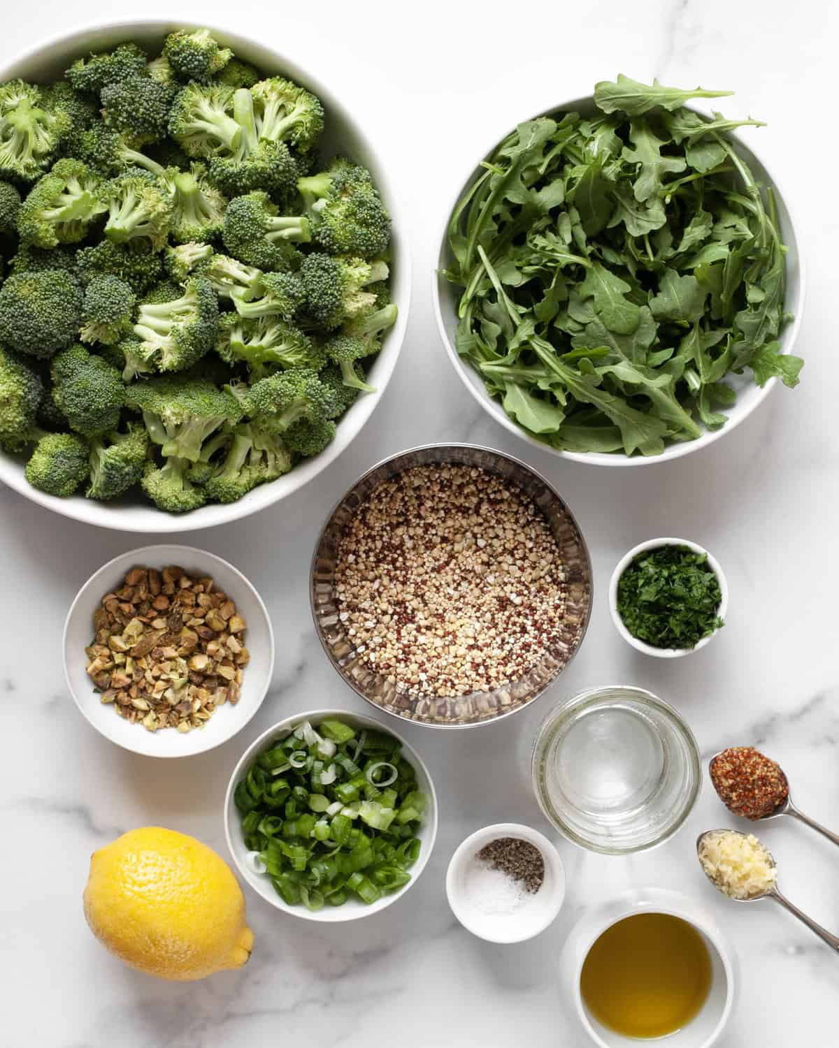 Ingredients including broccoli, quinoa, arugula, lemon, pistachios, parsley, garlic, mustard, oil an scallions.