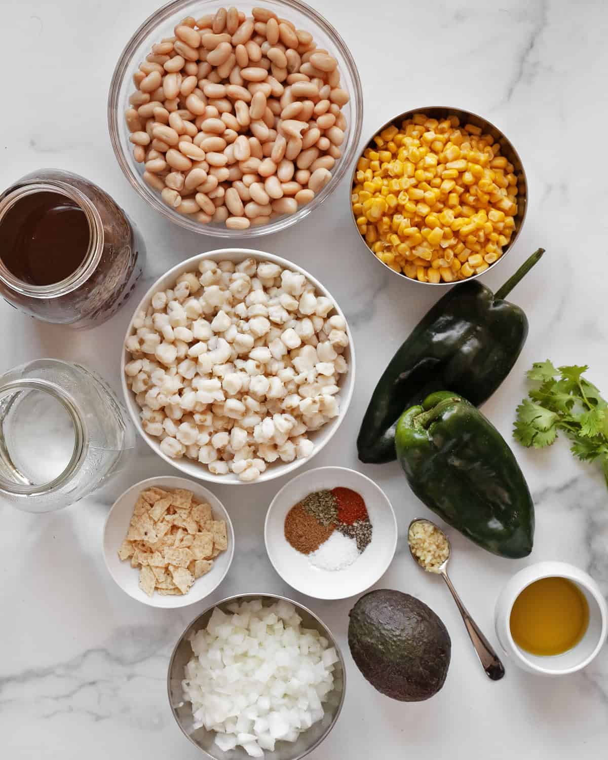 Ingredients including cannellini beans, corn, hominy, poblano peppers, onion, spices, broth, water, cilantro, avocado and tortilla chips.