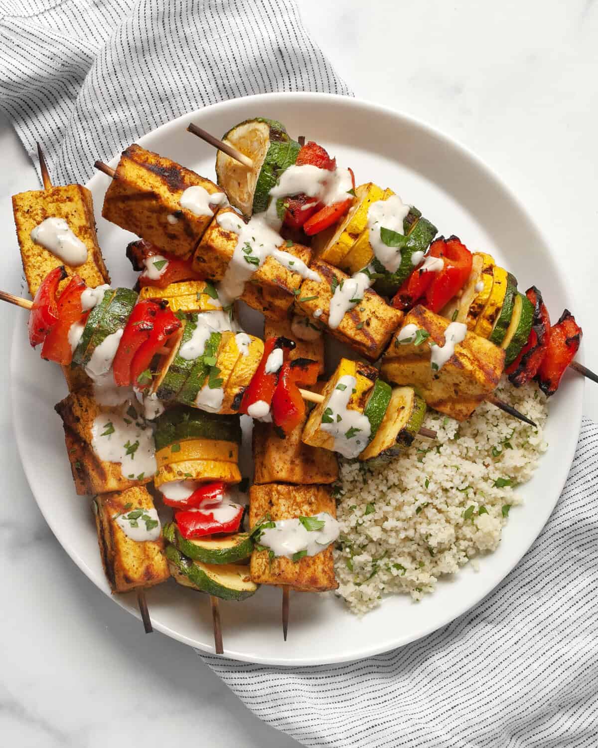 Grilled tofu and vegetable skewers with couscous on a plate.