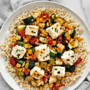 Baked feta with corn, tomatoes and zucchini with pearl couscous on a plate.