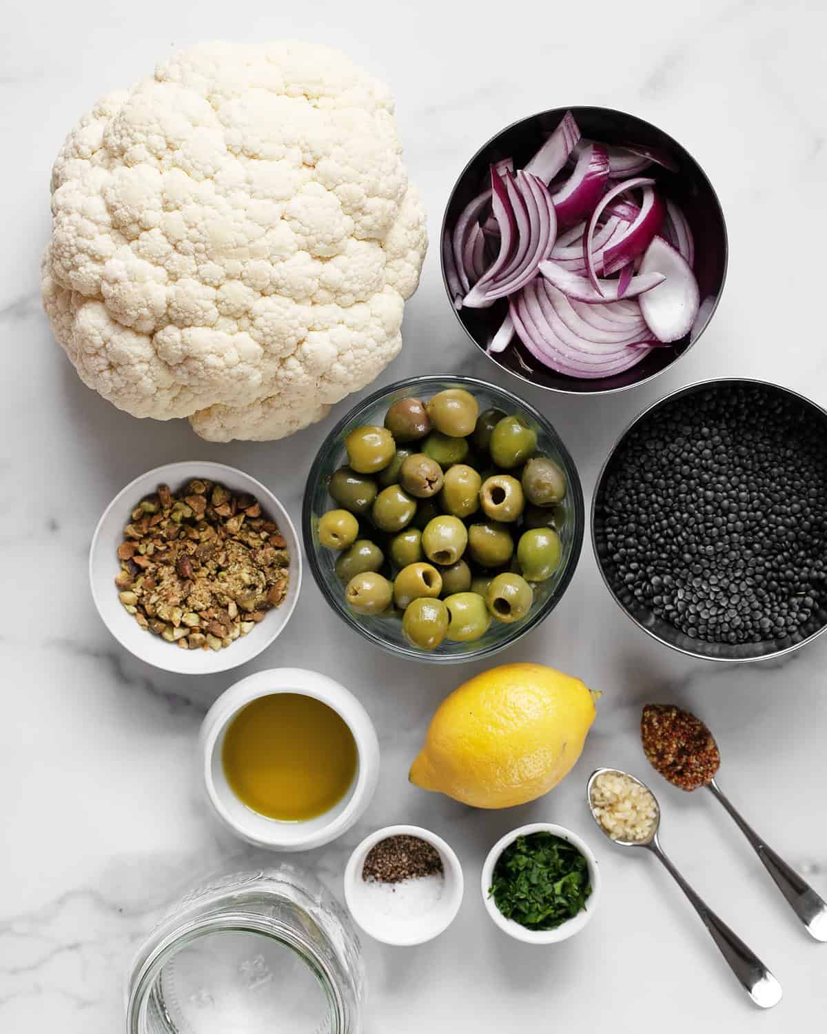 Ingredients including cauliflower, black lentils, olives, red onions, lemon, garlic, pistachios, olive oil, garlic and mustard.