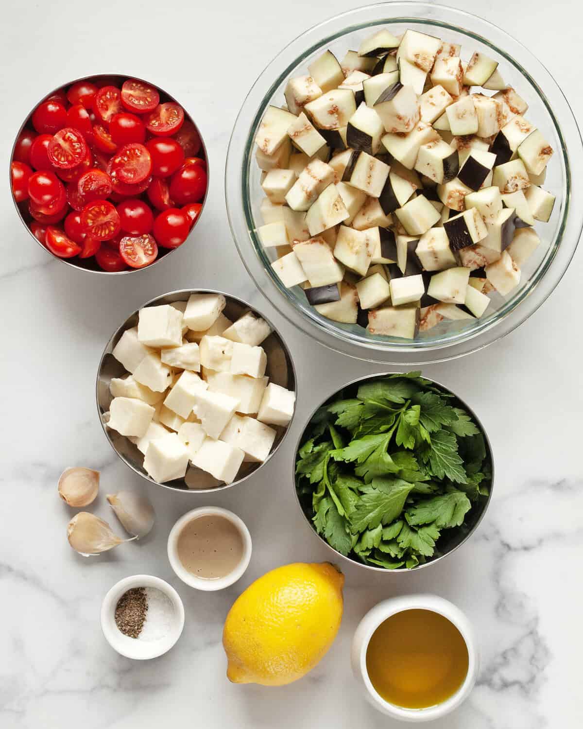 Ingredients including eggplant, tomatoes, halloumi, lemon, garlic, parsley, salt, pepper and olive oil.