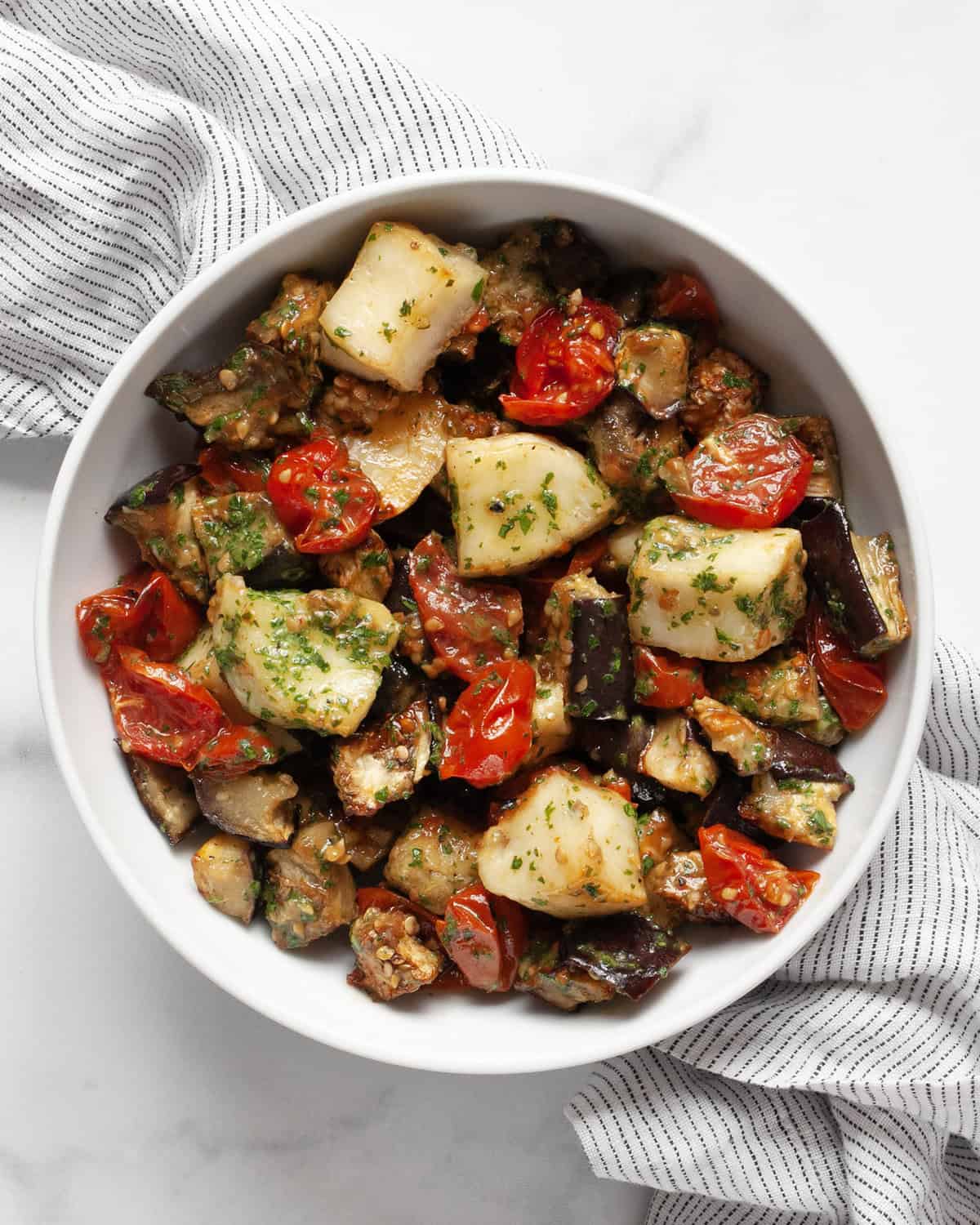 Roasted eggplant, tomatoes and halloumi in a bowl.