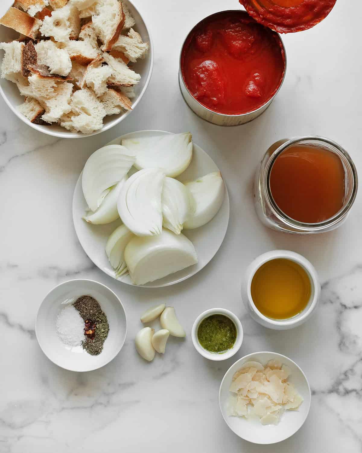 Ingredients including canned tomatoes, onions, garlic, veggie broth, seasonings, pesto, parmesan, bread and olive oil.