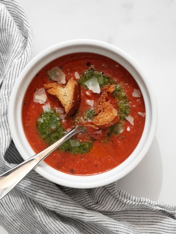 Bowl of tomato soup topped with pesto and croutons.