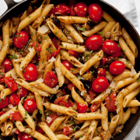 Penne pasta with cherry tomatoes and diced eggplant in a skillet.
