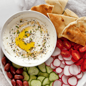 Greek yogurt labneh in a bowl with vegetables, olives and pita on a platter.