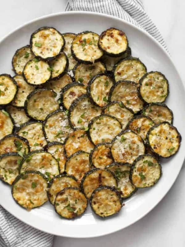 Roasted zucchini on a plate sprinkled with chopped parsley.