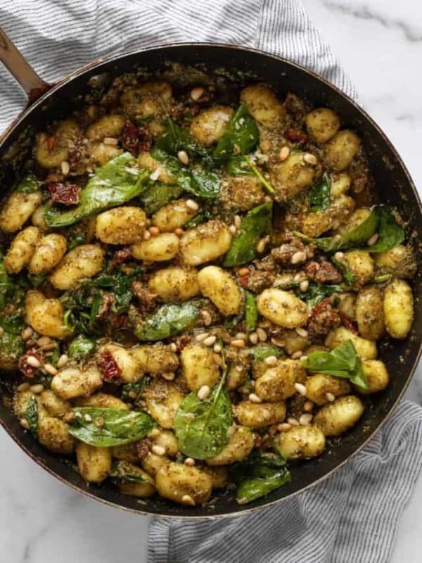 A large skillet with gnocchi, sun dried tomatoes and spinach simmered in pesto and fresh lemon juice.