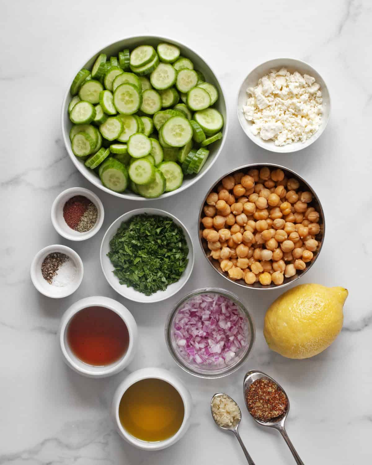 Ingredients including cucumbers, chickpeas, feta, parsley, lemon, red onions, olive oil, vinegar and spices.