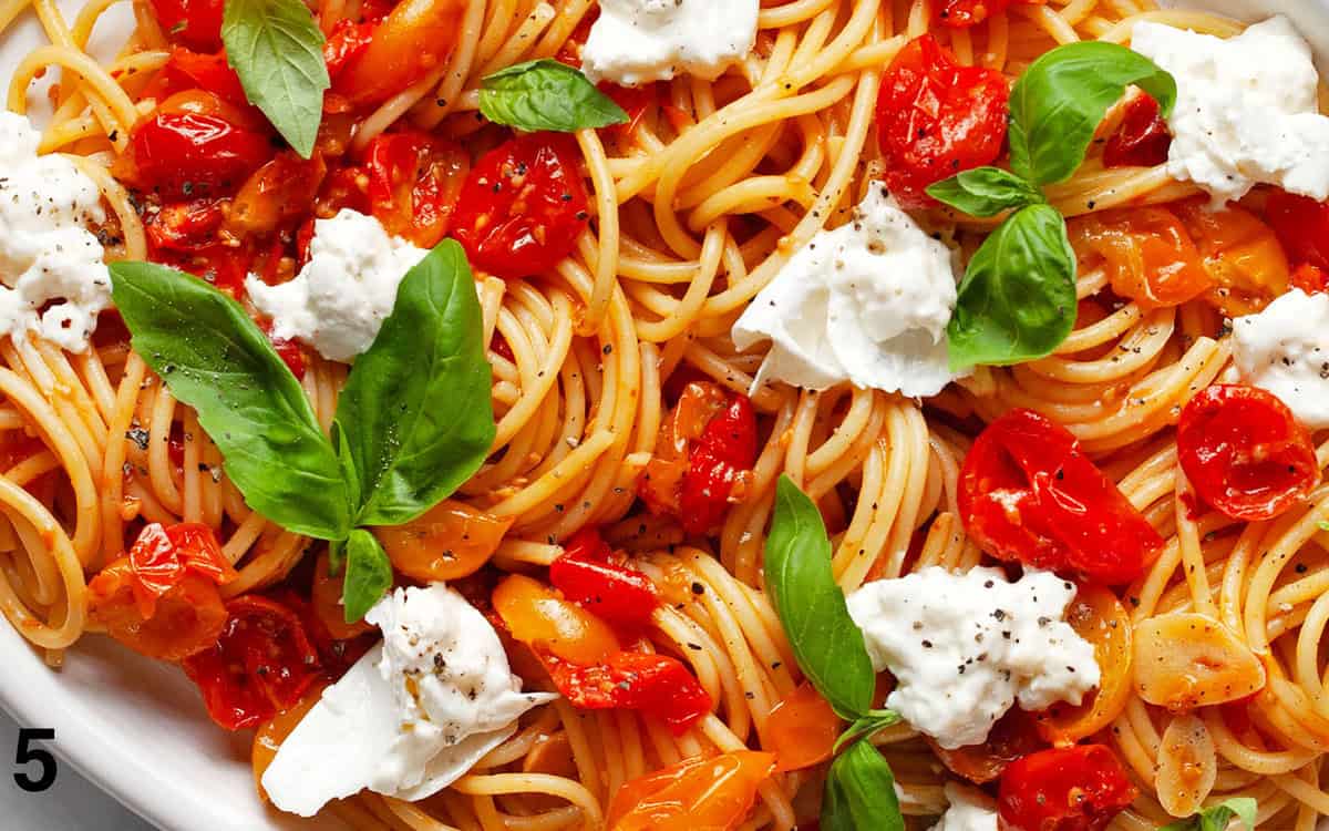 Pasta with roasted tomatoes, burrata and basil on a serving plate.