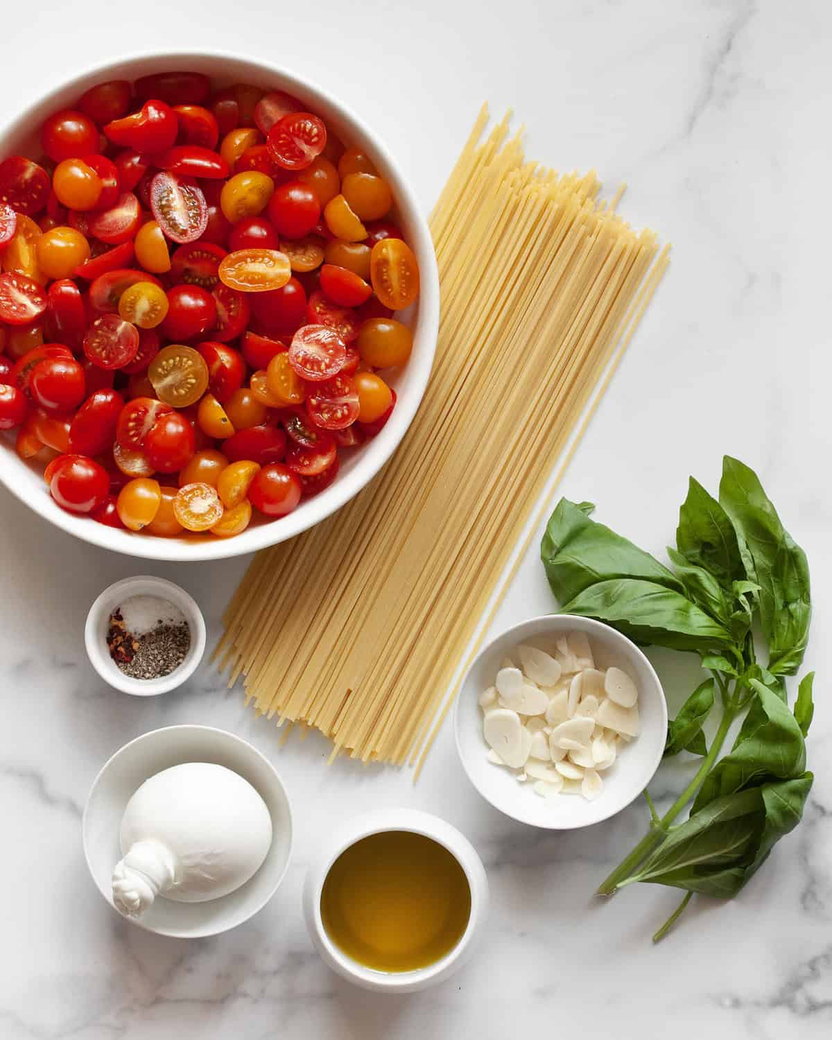 Ingredients including tomatoes, pasta, burrata, basil, olive oil, garlic and seasonings.