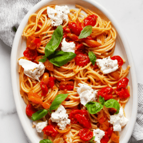 Spaghetti with roasted tomatoes, burrata and basil on an oval platter.