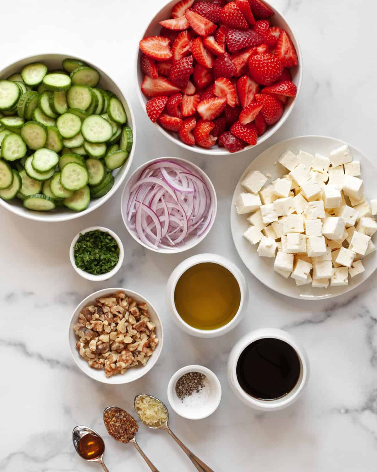 Ingredients including strawberries, feta, cucumbers, red onions, walnuts, parsley, balsamic vinegar, honey, olive oil, salt and pepper.