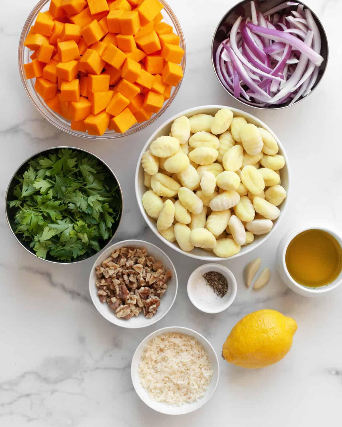 Ingredients including cubed butternut squash, sliced red onions, gnocchi, parsley, garlic, parmesan, walnuts, garlic, lemon, salt, pepper and olive oil.