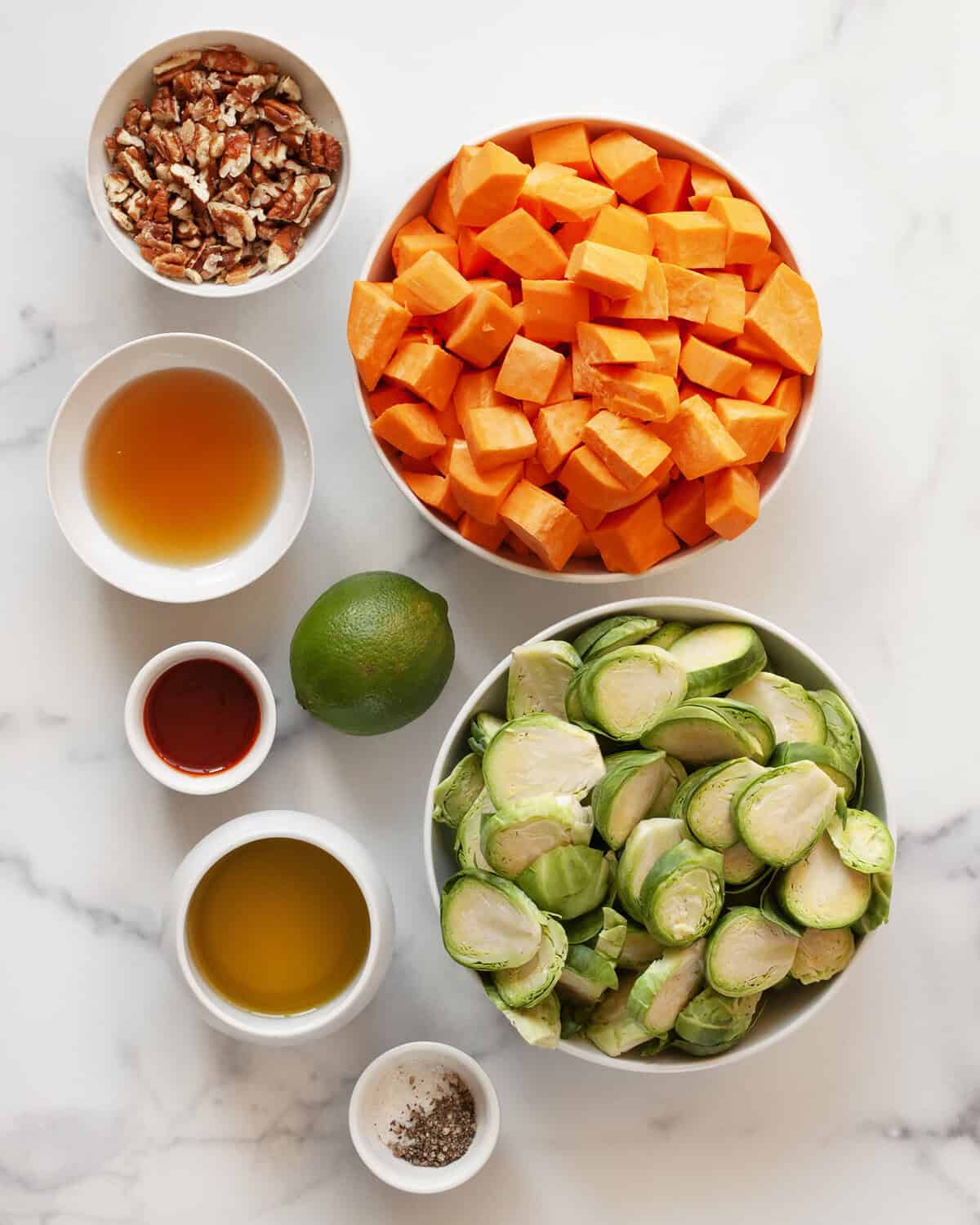 Ingredients including sweet potatoes, brussels sprouts, pecans, lime, olive oil, maple syrup, sriracha, salt and pepper.