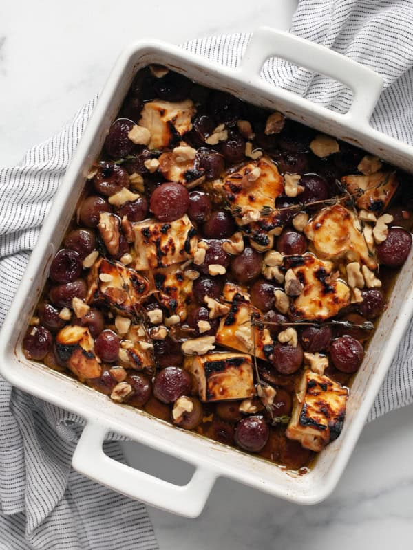 Baked feta and grapes in a dish with a serving spoon.